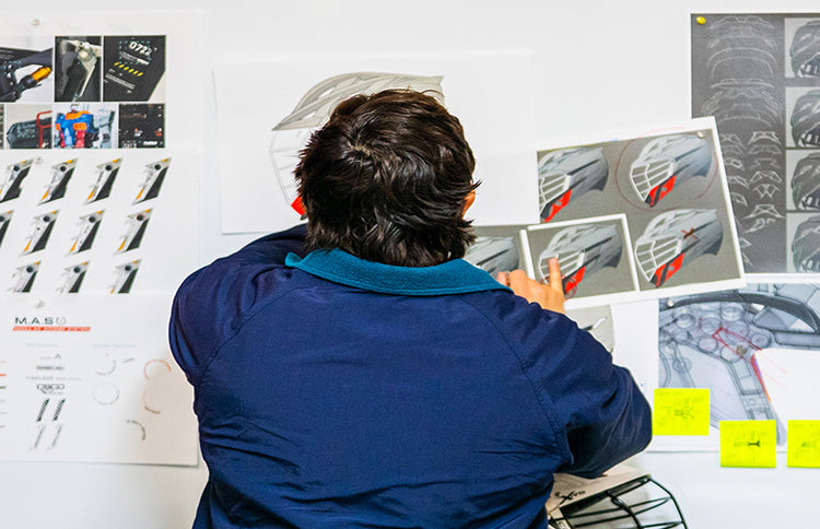 Person in a blue jacket looking at design sketches on a whiteboard with various Z HELMET parts.